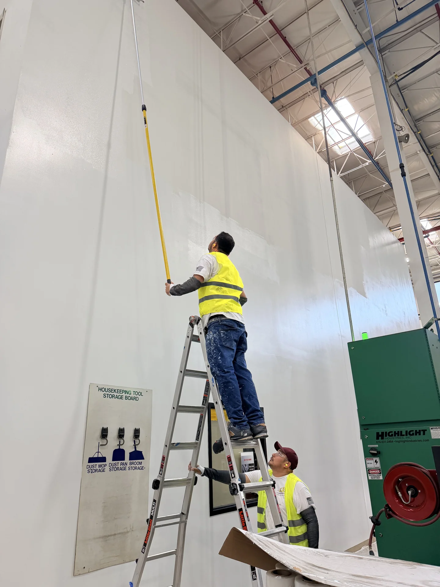 Crew painting a high-bay wall at a commercial metal facility