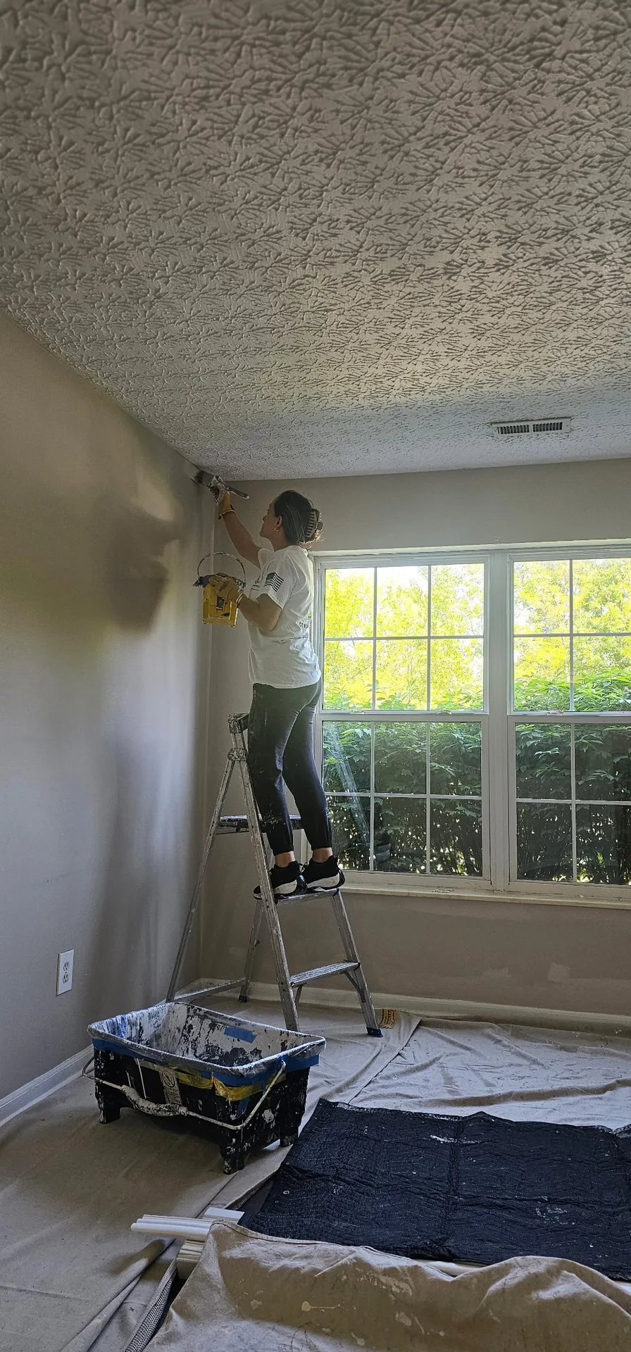 Painter carefully cutting in a ceiling line on a ladder
